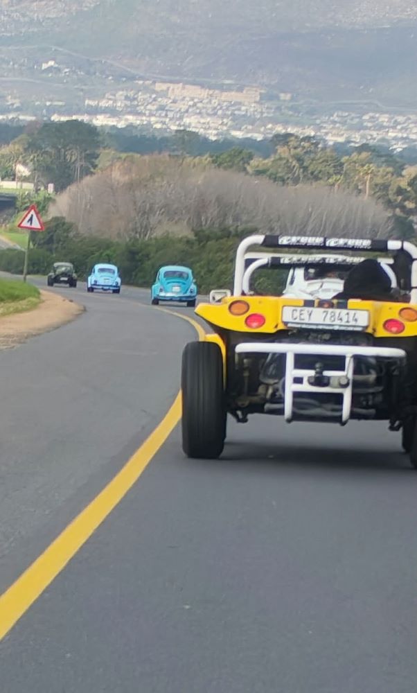 The Wild Buggers convoy on the open road featuring a yellow Beamish Beach Buggy, classic VW air-cooled Beetles, and a Baja Bug heading toward the secret breakfast stop.