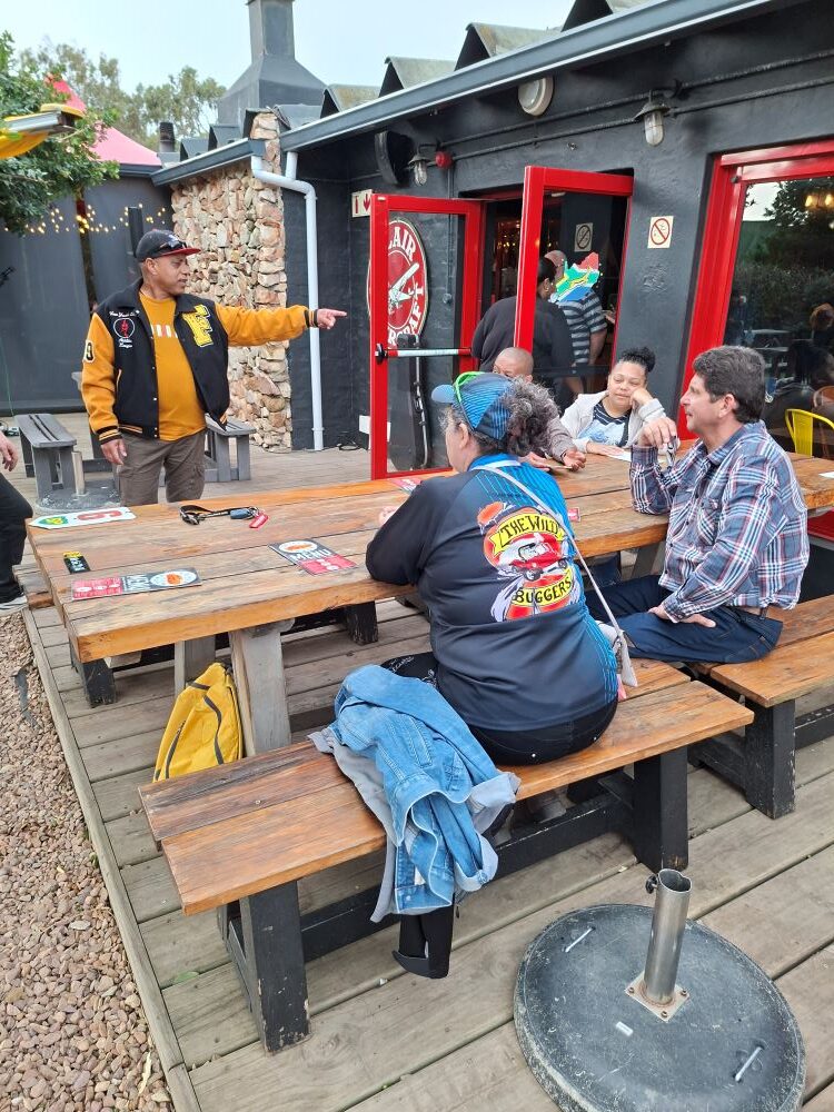 Club members relaxing and chatting at wooden tables on the patio while waiting for ice cream during the stop.