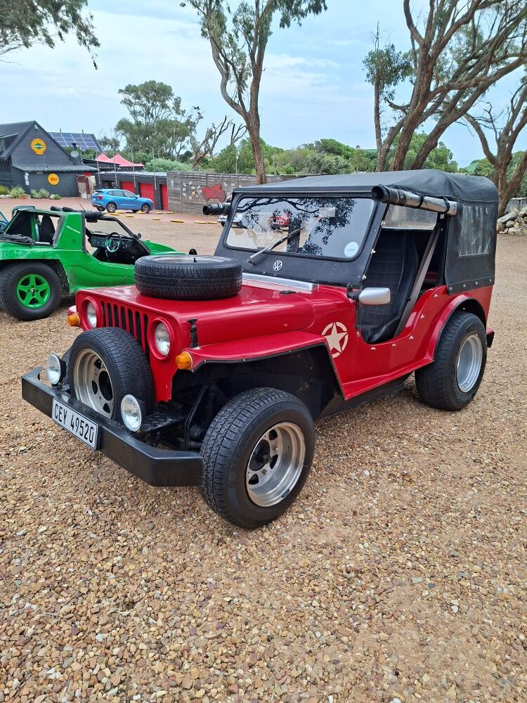 A red custom beach buggy styled like a vintage military Jeep parked alongside other vehicles during the club run.