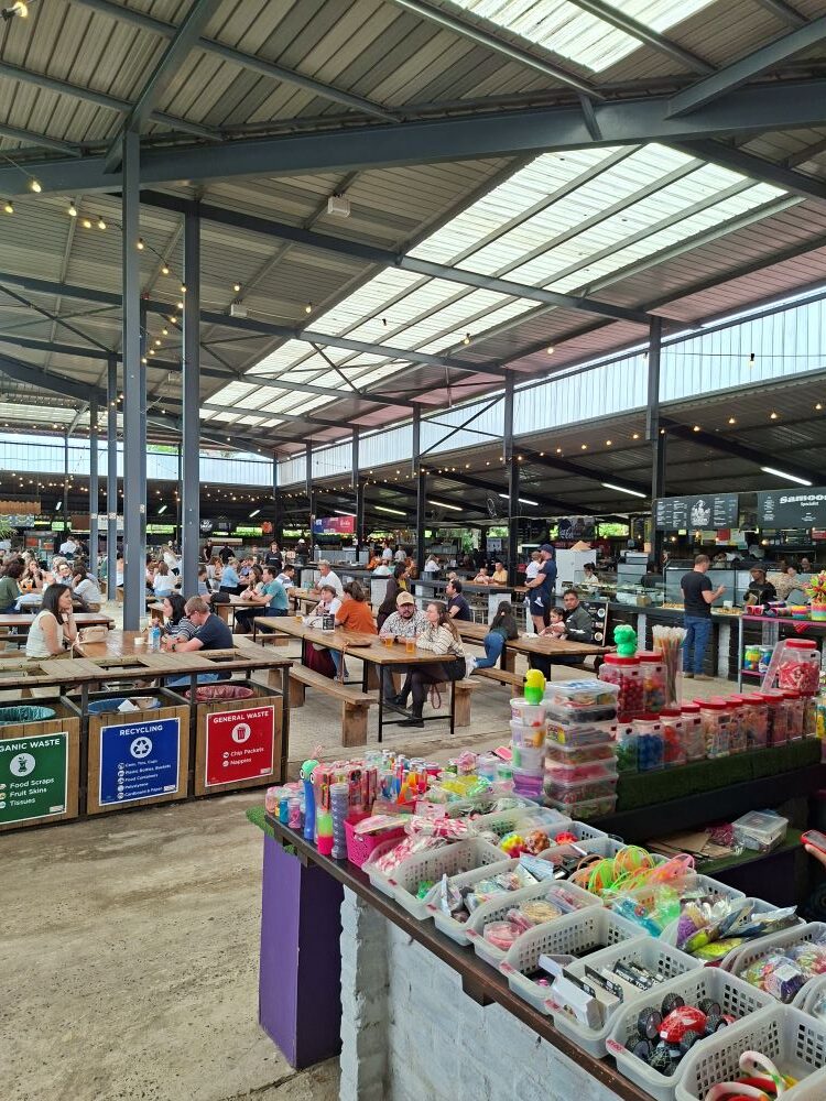 Colorful display stalls and bustling seating areas inside the busy hall at Lourensford Market.