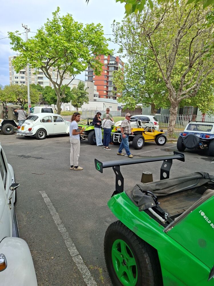Club members chatting next to a parked green beach buggy and classic air-cooled VW cars in the parking lot.