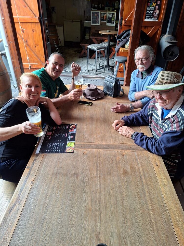 Club members raising glasses for a cheerful toast while seated at a rustic wooden table and reviewing menus during the stop.
