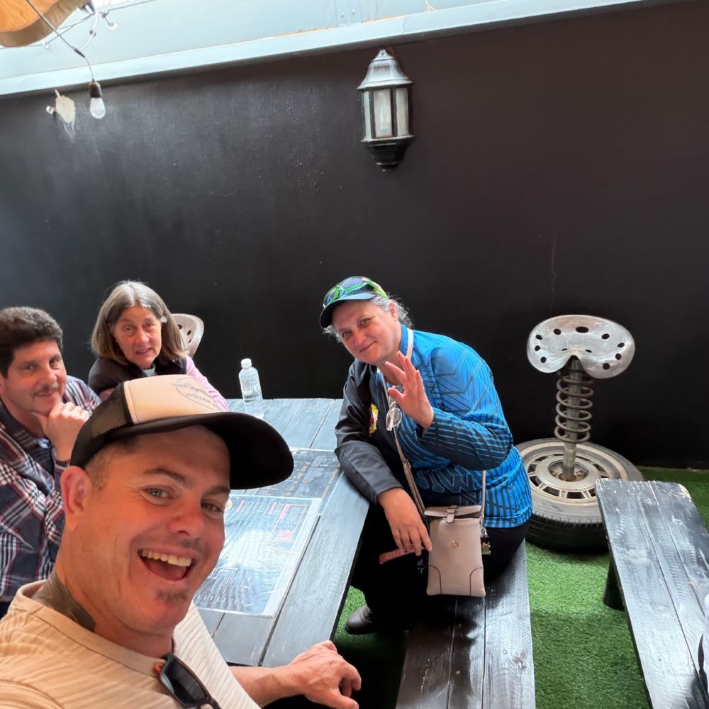 Neil takes a cheerful group selfie with club members smiling and waving at the restaurant during the lunch stop