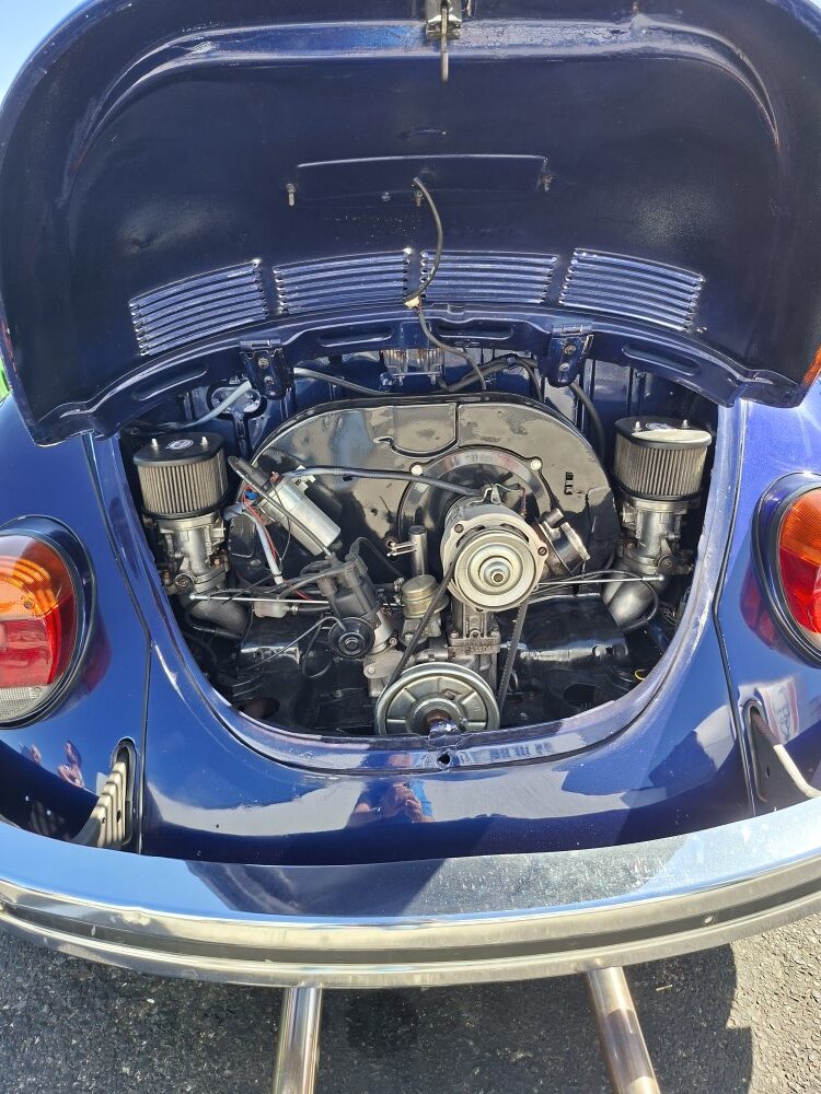 A detailed close-up of a neatly tuned dual-carburetor engine inside the open rear decklid of a classic air-cooled VW Beetle.