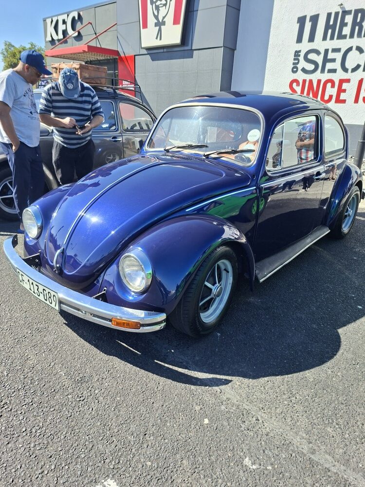 A high-angle view of a gleaming dark blue classic Beetle parked outside Bothasig KFC during a club meetup.