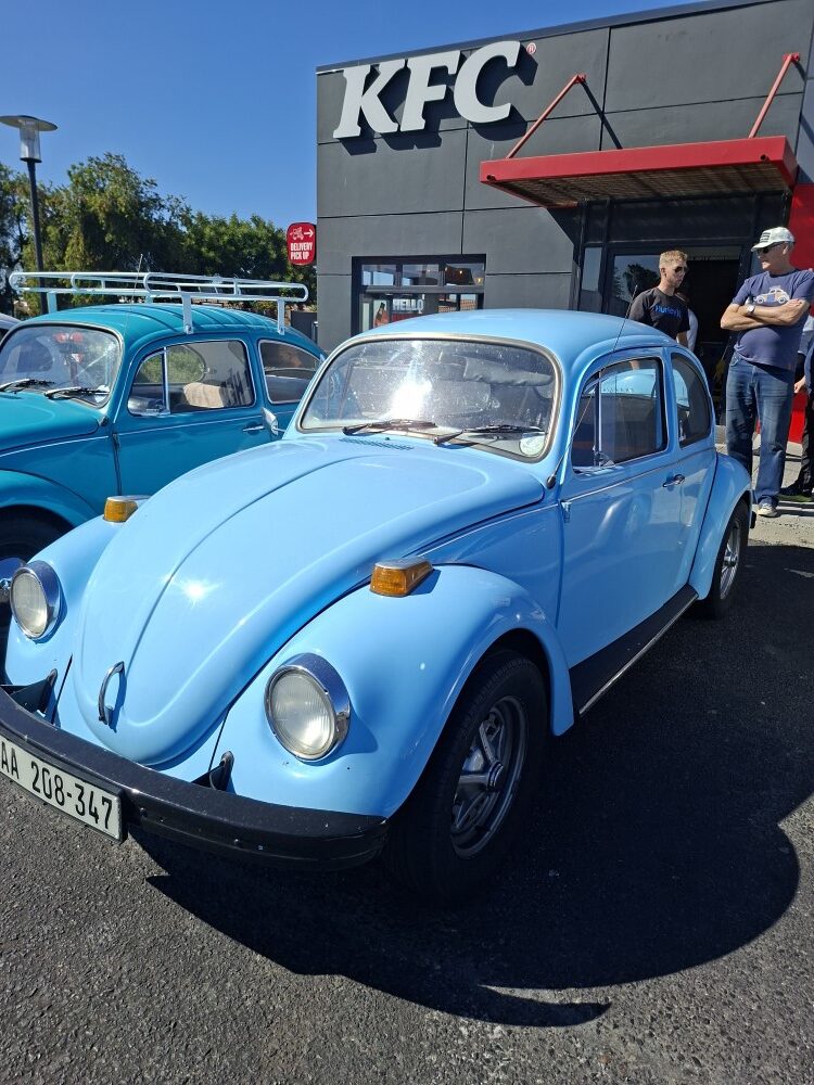 A light blue 1974 classic VW Beetle parked outside Bothasig KFC during a club run meetup.