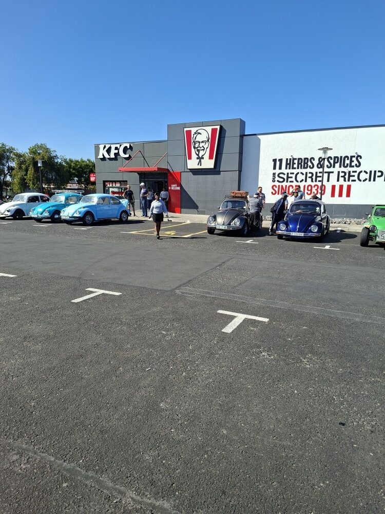 A gathering of classic air-cooled VW Beetles and a beach buggy in the Bothasig KFC parking lot before a club run.