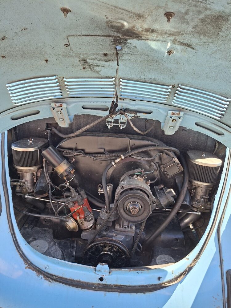 A close-up view inside the open engine bay of a light blue classic VW showing a dual-carburetor air-cooled motor setup.