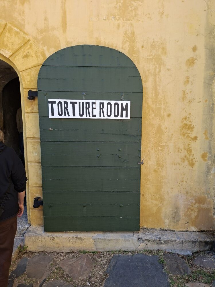 A heavy wooden green arched door mounted on a historic stone wall with a sign reading Torture Room.