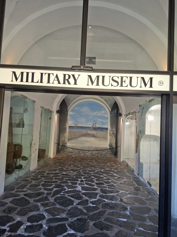 A glass doorway with sign text reading Military Museum leading into a stone paved hallway inside the Castle.