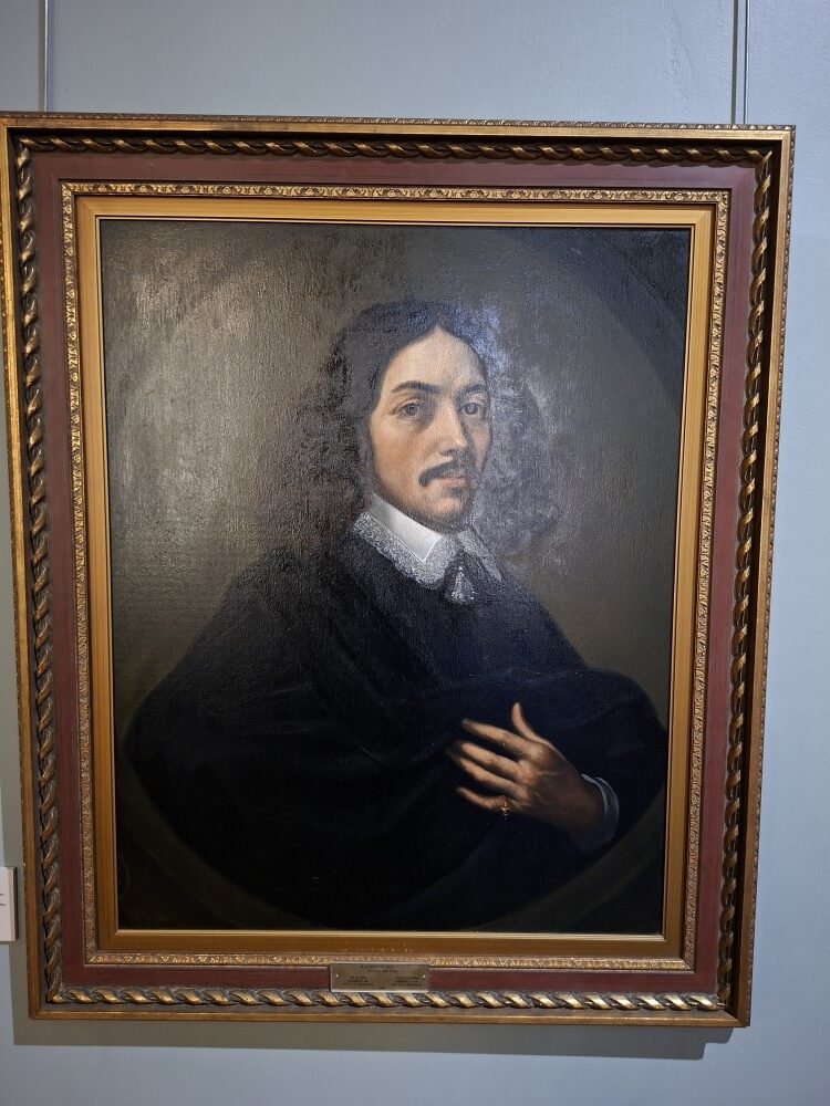 A framed historical oil painting portrait of Jan van Riebeeck hanging inside a museum gallery wall.
