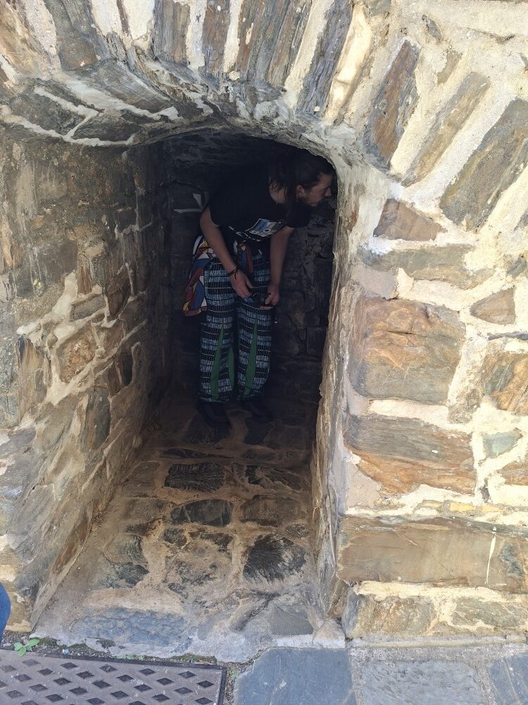 A man ducking down to peer into a low, stone-paved vaulted archway tunnel inside a historic fort.