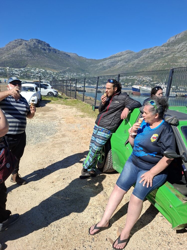 Mickey, Jacques, and Leon Visser enjoying ice cream cones while leaning against the bright green beach buggy Shrek at the harbour.